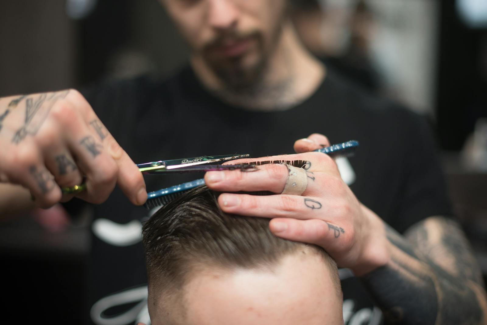 A tattooed barber provides a precise haircut in a modern barbershop setting.