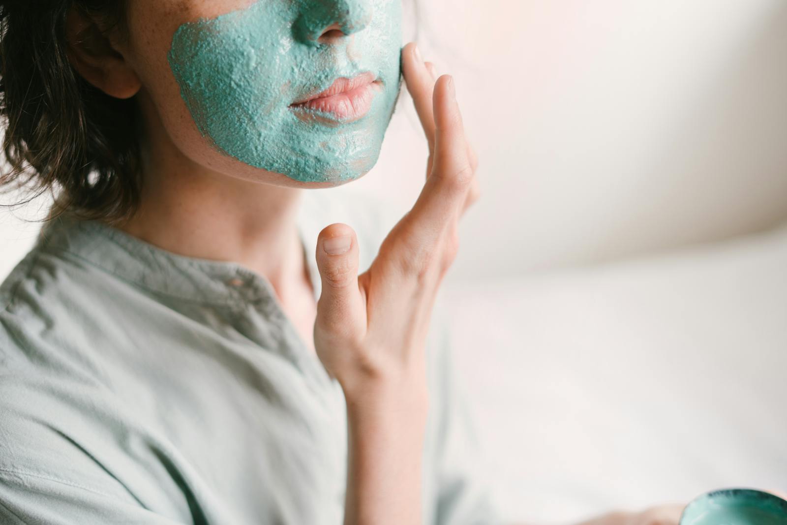 Young woman applies a rejuvenating facial mask indoors for skin care and relaxation.