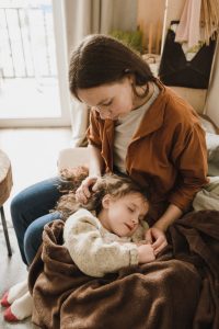 A mother gently caresses her sleeping daughter on a cozy couch indoors.