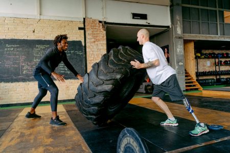 Adaptive athlete with prosthetic leg flipping tire during intense gym workout.